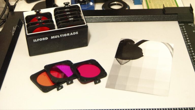 workspace showing various colored filters used in the process of split grade printing in a photo darkroom